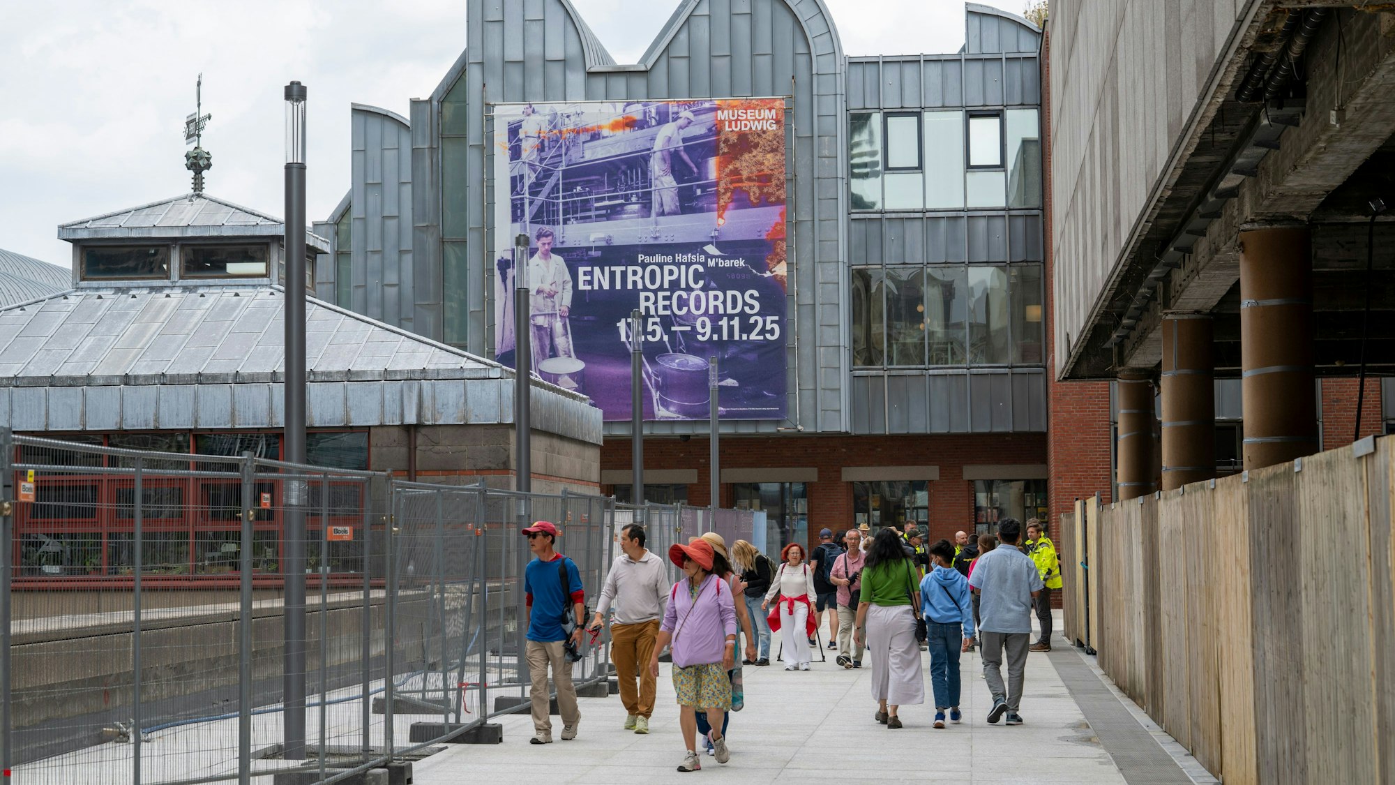 Menschen laufen vorbei an Bauzäunen über einen Weg.