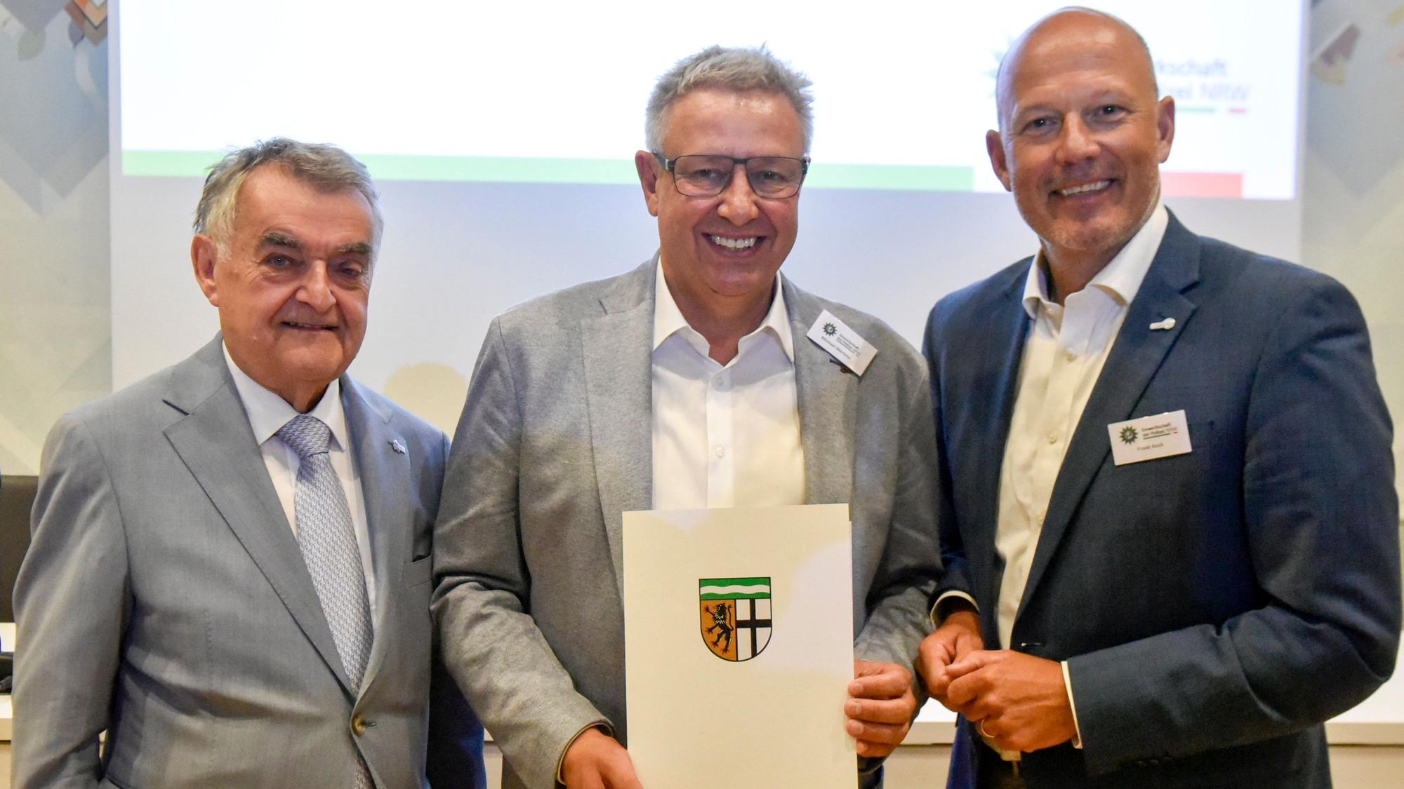 Das Bild zeigt drei Männer, einer hält eine Urkunde in seinen Händen.