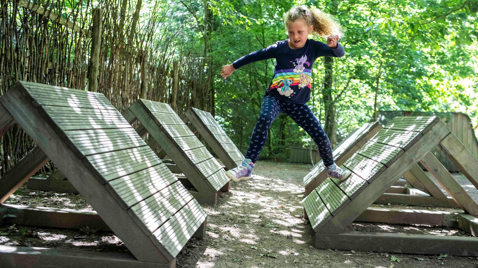 Ein Mädchen springt im Arboretum in Nettersheim durch einen Parcours mit schräggestellten Holz-Hindernissen.