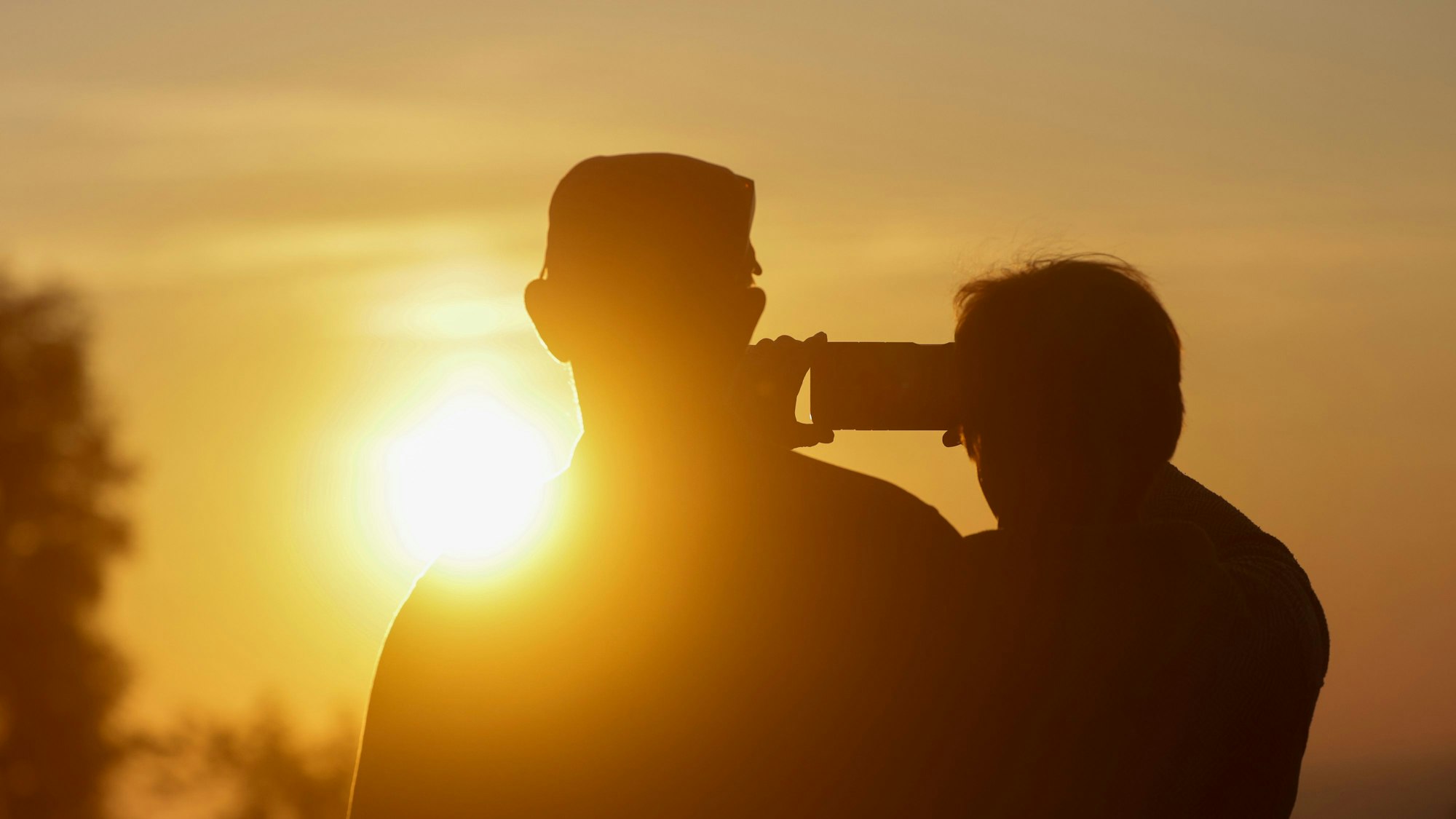 Ein Mann und eine Frau fotografieren mit einem Handy den Sonnenaufgang.