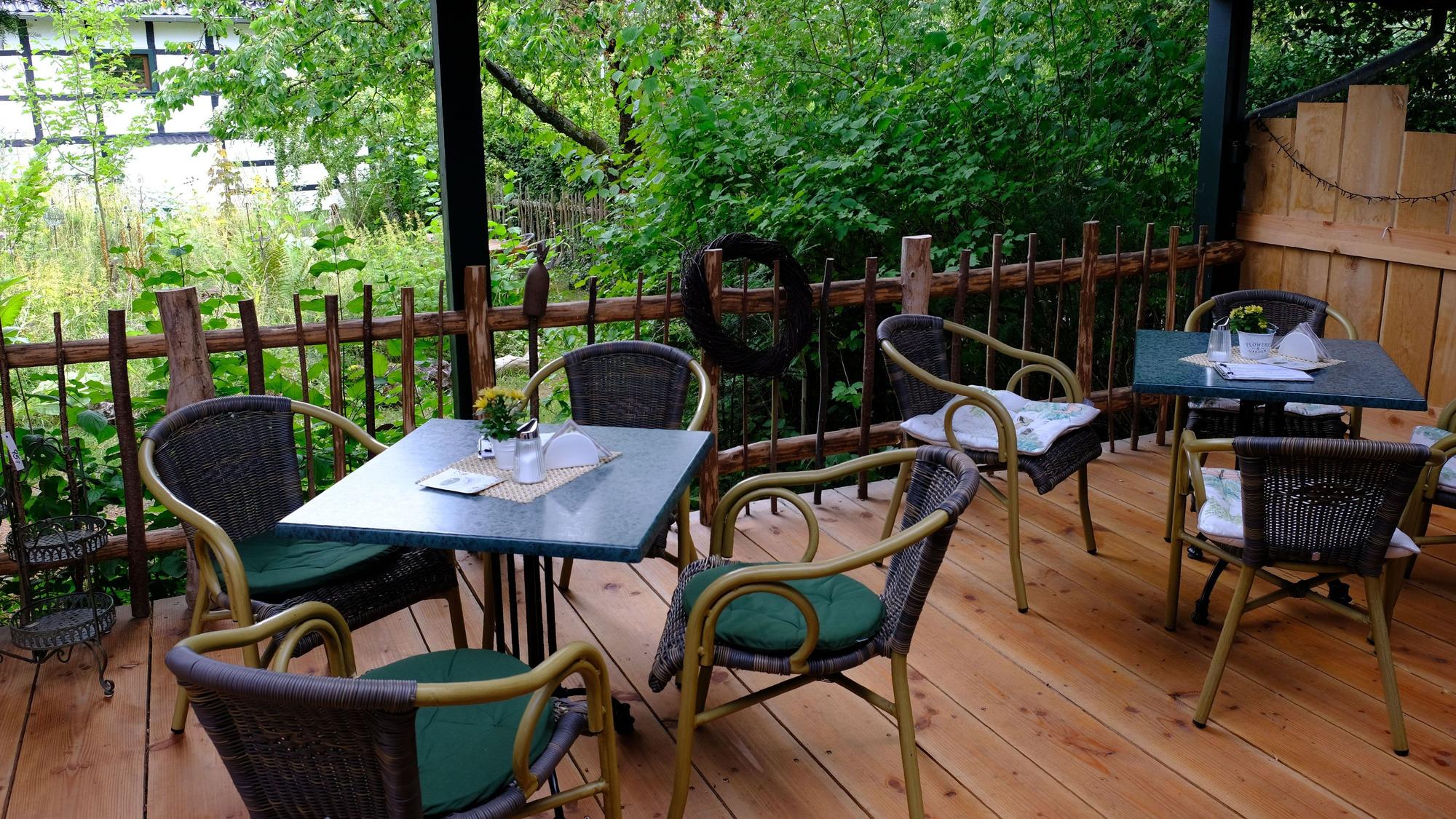 Blick von der überdachten Terrasse, wo Tische und Stühle stehen, in den Garten.