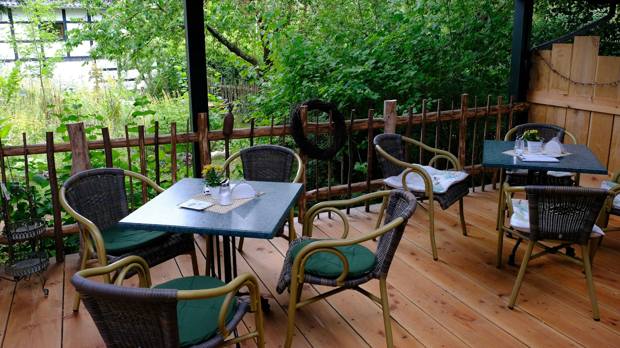 Blick von der überdachten Terrasse, wo Tische und Stühle stehen, in den Garten.