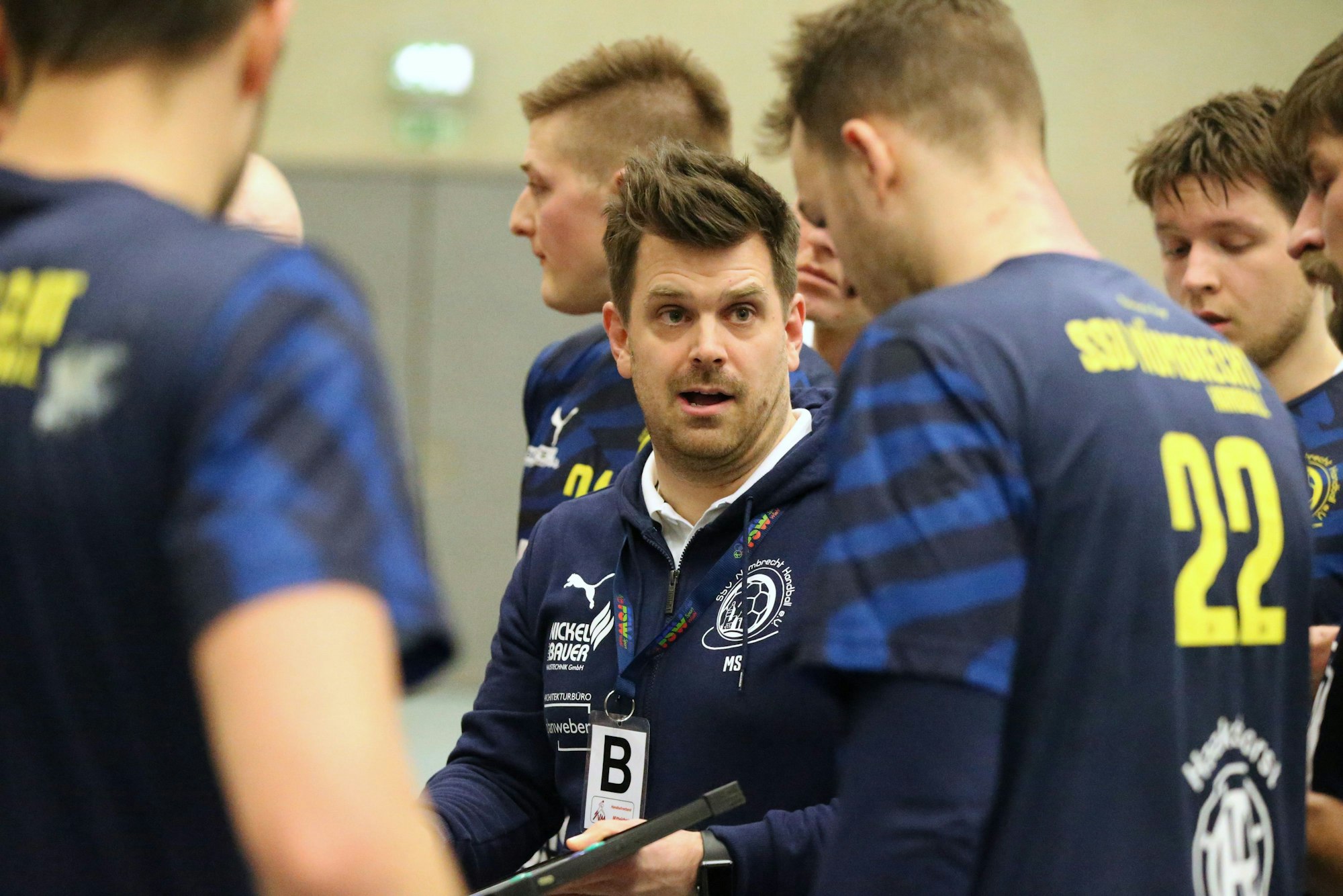 Ein Handballtrainer steht in einer Halle umgeben von seinen Spielern.