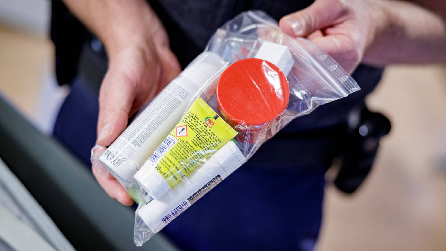 Ein Sicherheitsbeamter zeigt Flüssigkeiten in einem transparenten, wiederverschließbaren Plastikbeutel.
