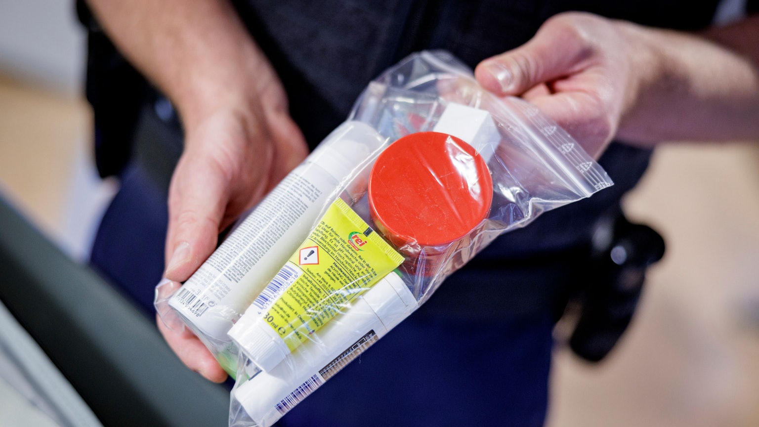 Ein Sicherheitsbeamter zeigt Flüssigkeiten in einem transparenten, wiederverschließbaren Plastikbeutel.