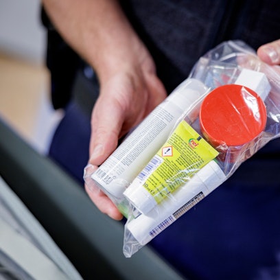 Ein Sicherheitsbeamter zeigt Flüssigkeiten in einem transparenten, wiederverschließbaren Plastikbeutel.