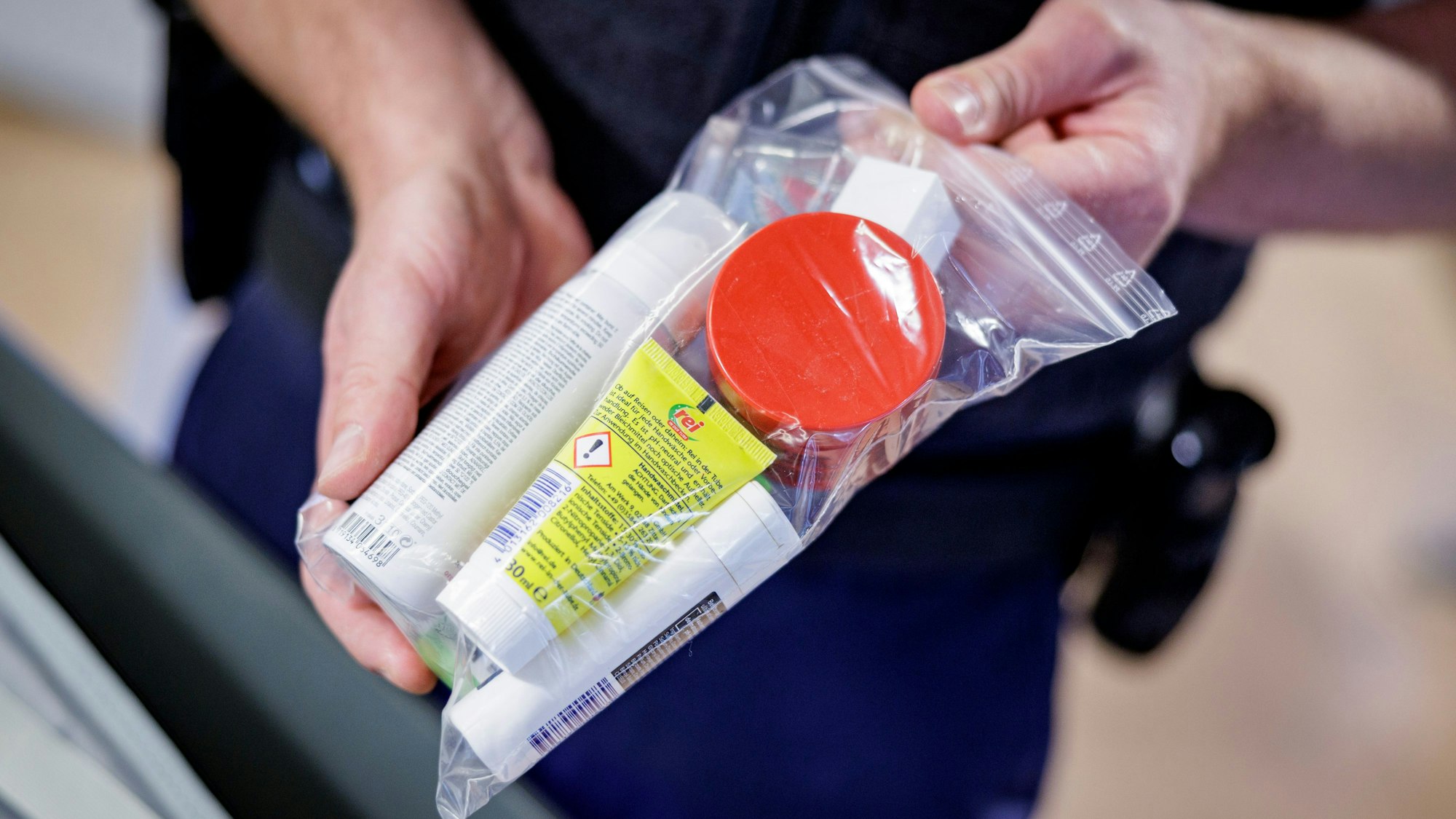 Ein Sicherheitsbeamter zeigt Flüssigkeiten in einem transparenten, wiederverschließbaren Plastikbeutel.
