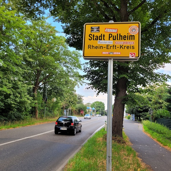 Ein Schild mit dem Schriftzug Stadt Pulheim mit vielen Aufklebern von FC-Fans.