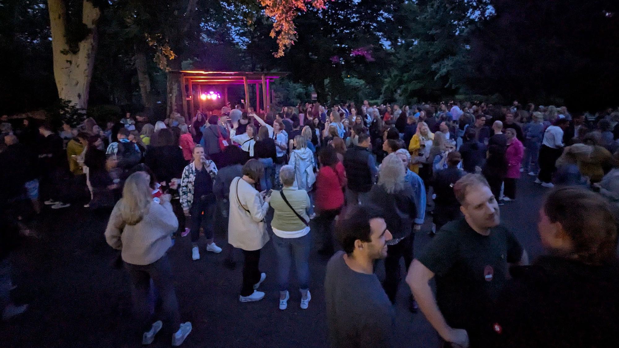 Menschen stehen auf einer Fläche vor einem DJ-Pult