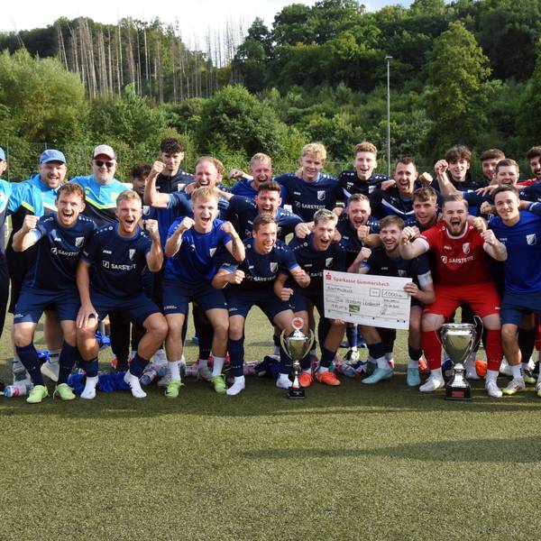 Eine jubelnde Fußballmannschaft mit Pokal und einem Scheck der Sparkasse Gummersbach über 100 Euro.