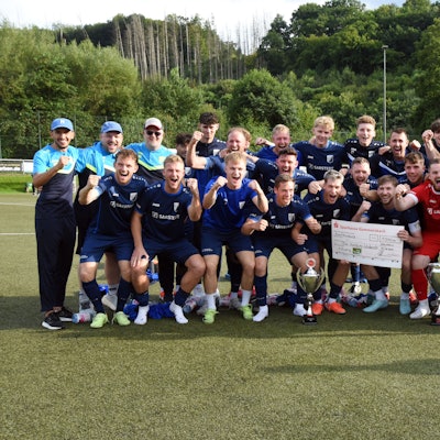Eine jubelnde Fußballmannschaft mit Pokal und einem Scheck der Sparkasse Gummersbach über 100 Euro.