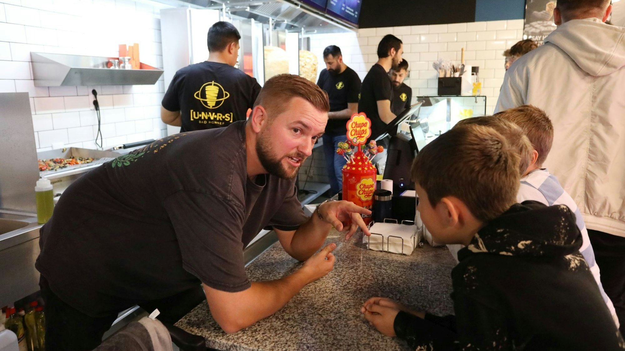 Ein Mann spricht in einem Döner-Imbiss mit drei Jungen.