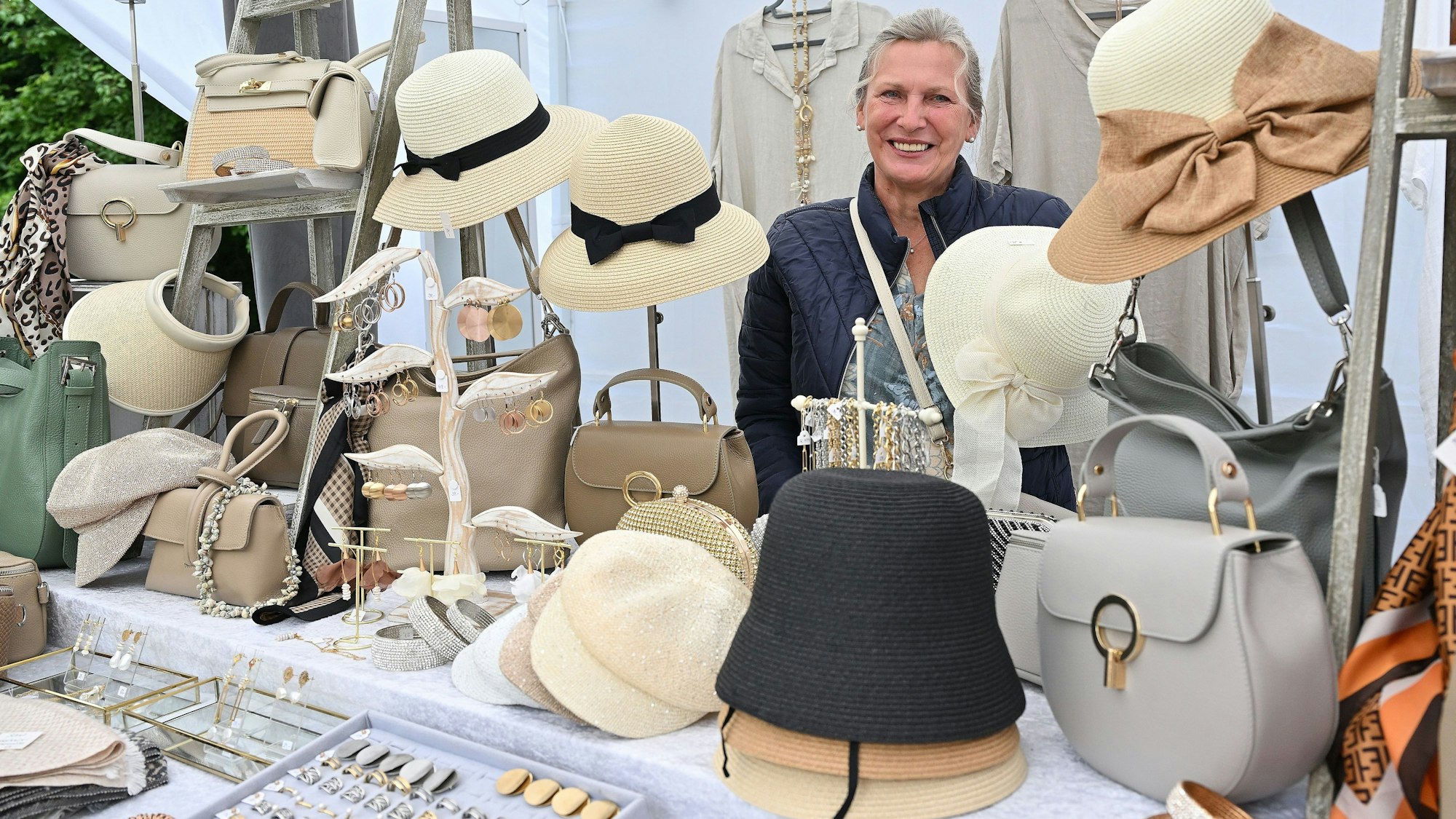 Ein Stand mit Hüten, Taschen und Schmuck; die Verkäuferin im Hintergrund.