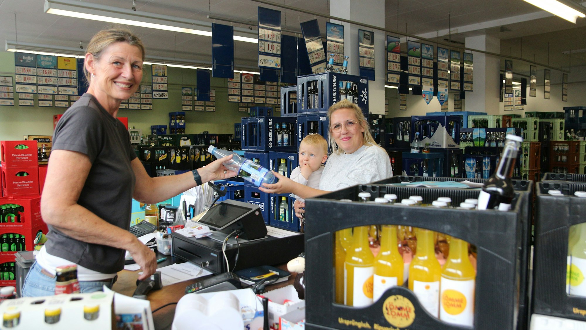 Das Foto zeigt zwei Frauen im Getränkeladen, eine trägt einen kleinen Jungen auf dem Arm.