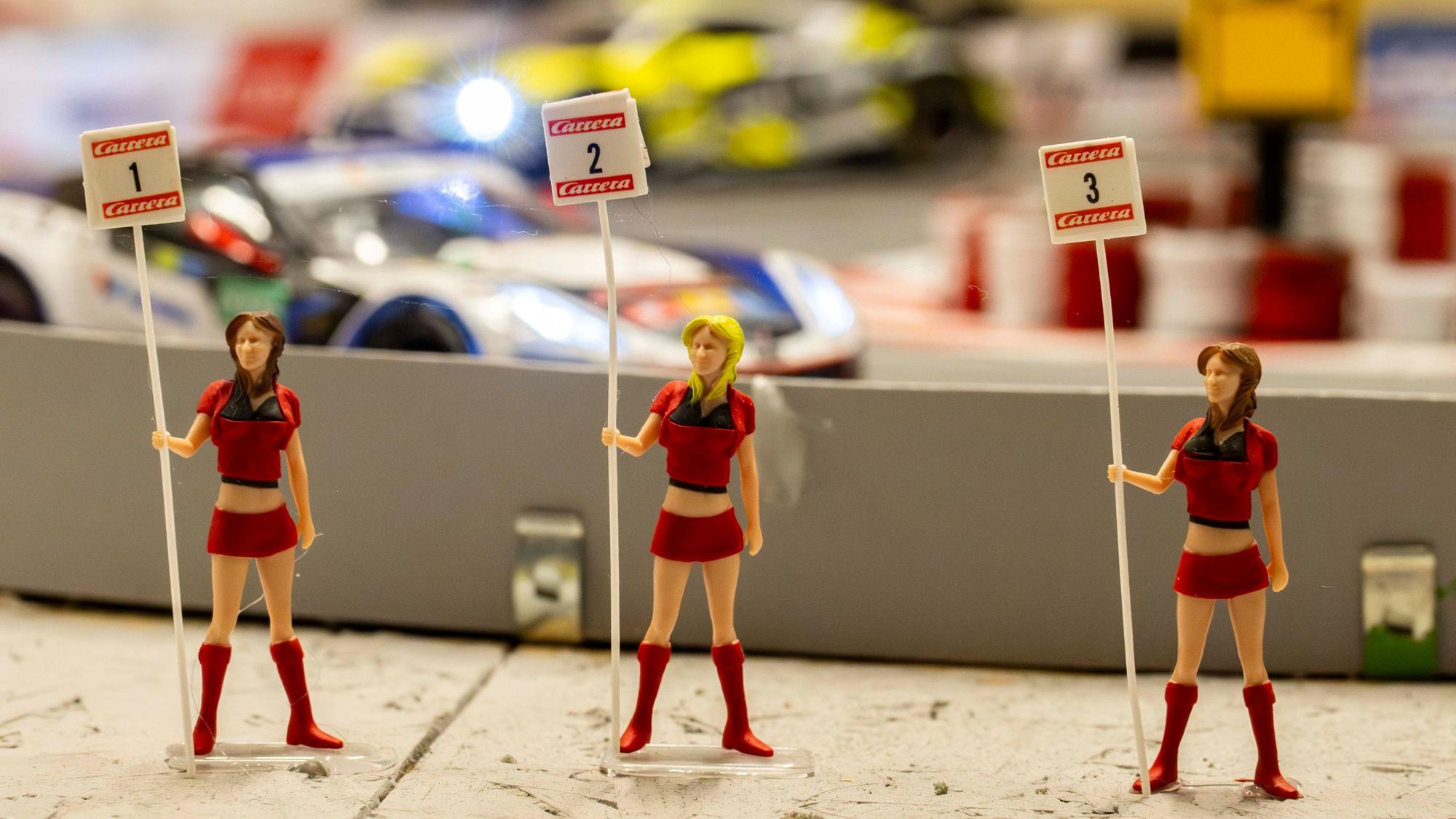 Vor der Carrera-Rennbahn stehen drei rot gekleidete Miniatur-Gridgirls.