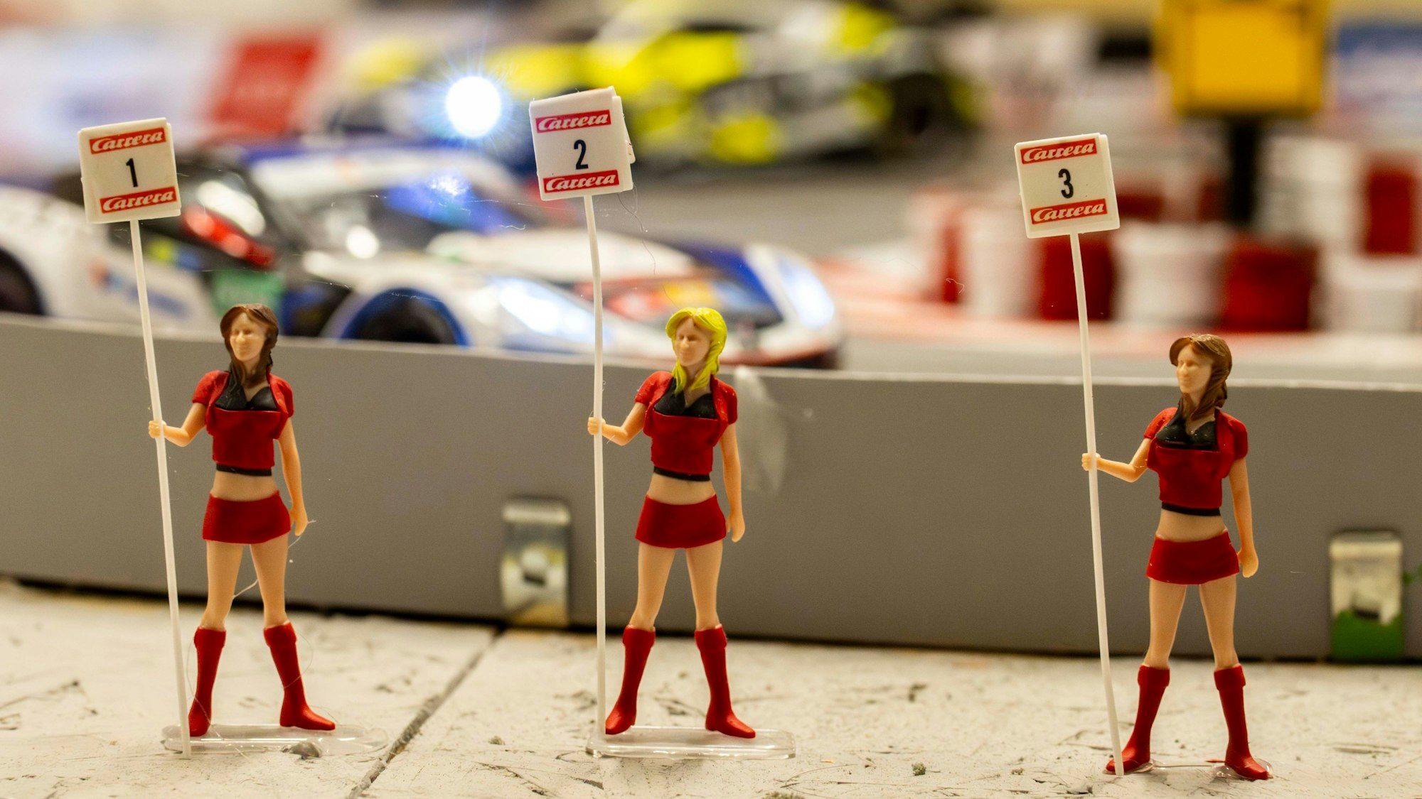 Vor der Carrera-Rennbahn stehen drei rot gekleidete Miniatur-Gridgirls.