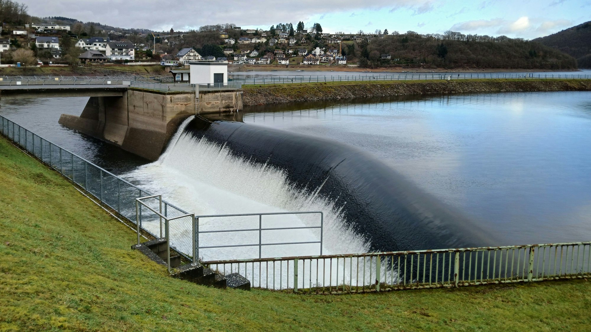 Wasser strömt aus dem Obersee in die Rurtalsperre. Im Hintergrund ist Rurberg zu sehen.