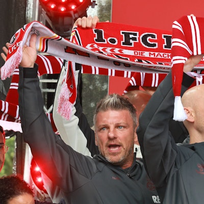 Kwasniok steht auf der Bühne und hält einen Schal nach oben.