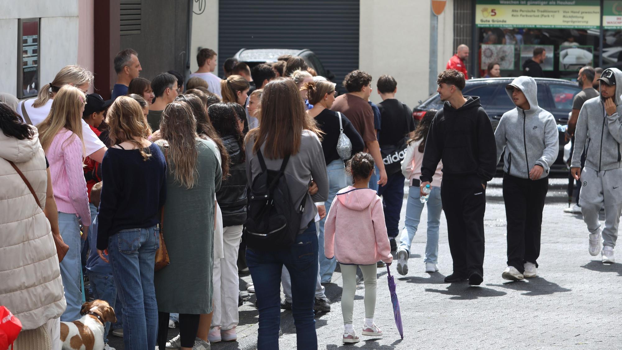 Menschen stehen in einer langen Schlange auf einem Gehweg und der Straße.