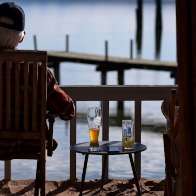 Ein Ausflügler sitzt in einem Biergarten am Ammersee im Sonnenschein, neben ihm steht ein Bier auf einem Tisch.