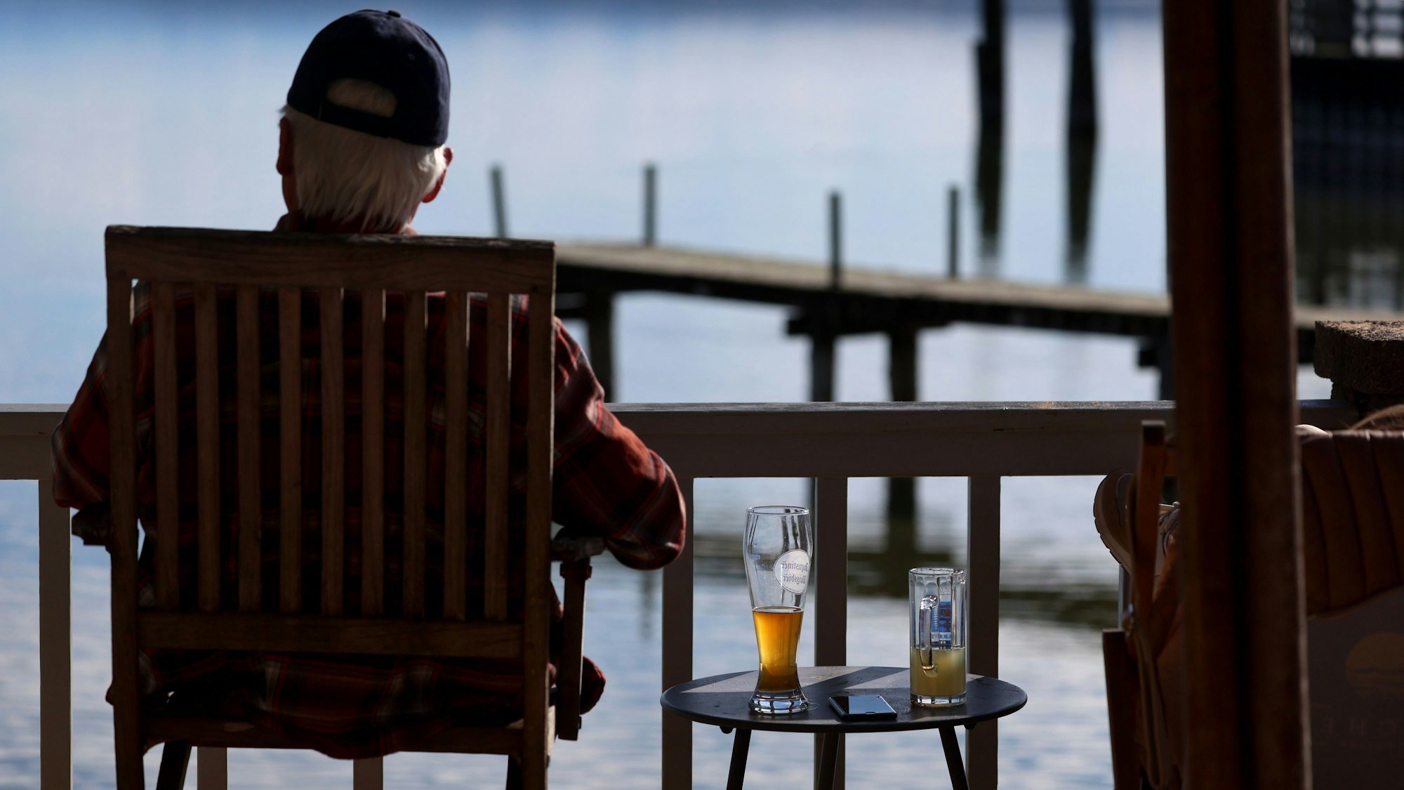 Ein Ausflügler sitzt in einem Biergarten am Ammersee im Sonnenschein, neben ihm steht ein Bier auf einem Tisch.