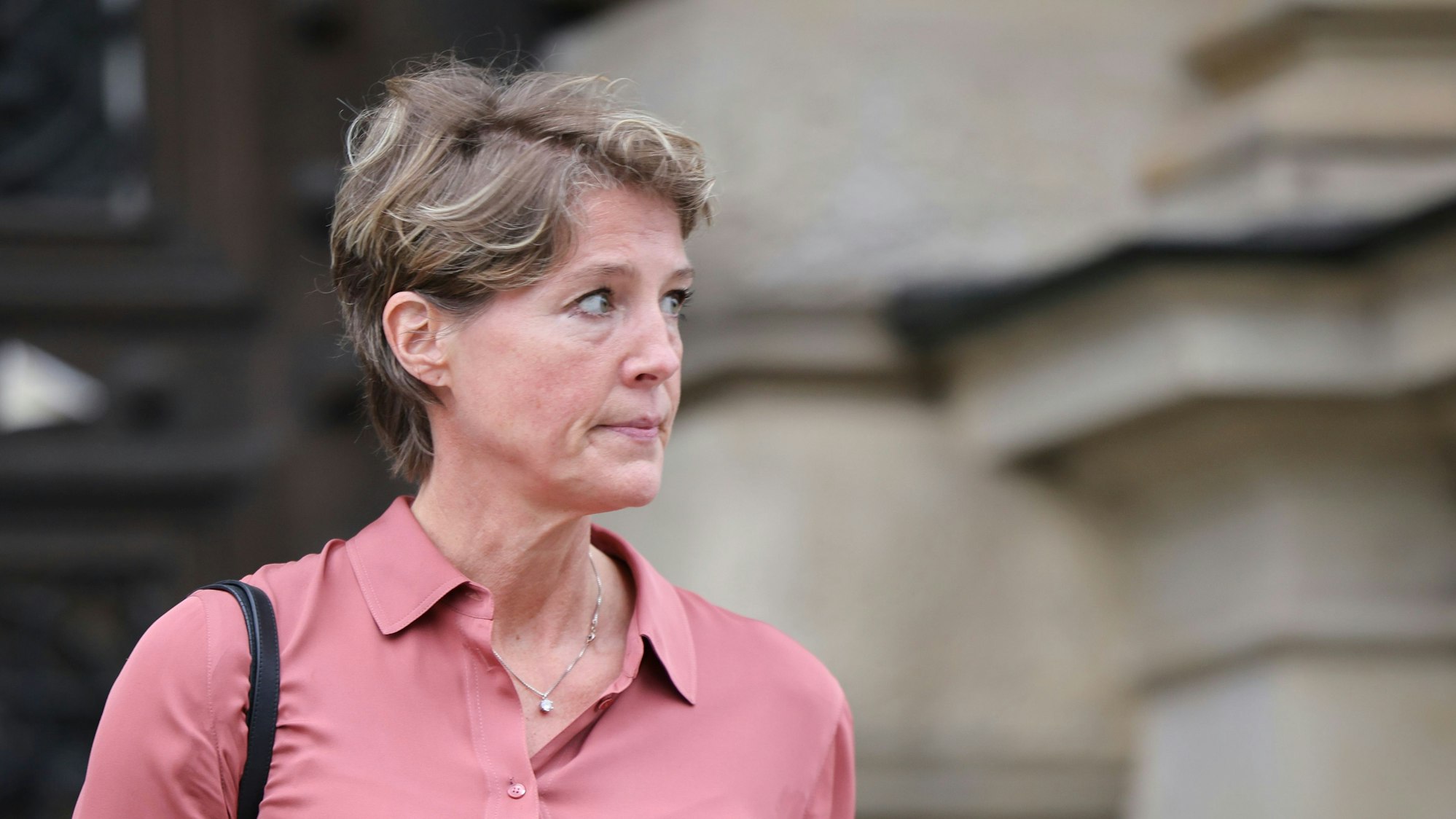 Christina Block schaut auf etwas, das außerhalb des Bildausschnittes liegt. Im Hintergrund befindet sich das unscharf gestellte Strafjustizgebäude in Hamburg.
