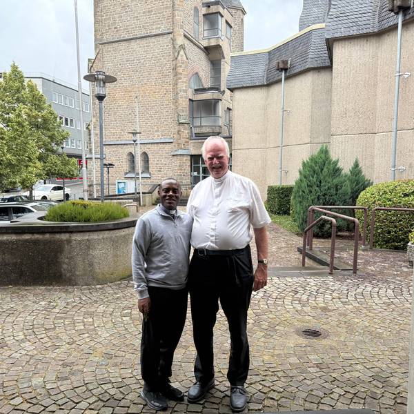 Pater Domisias Kayemba und Kreisdechant Christoph Bersch stehen vor einer Kirche nebeneinander