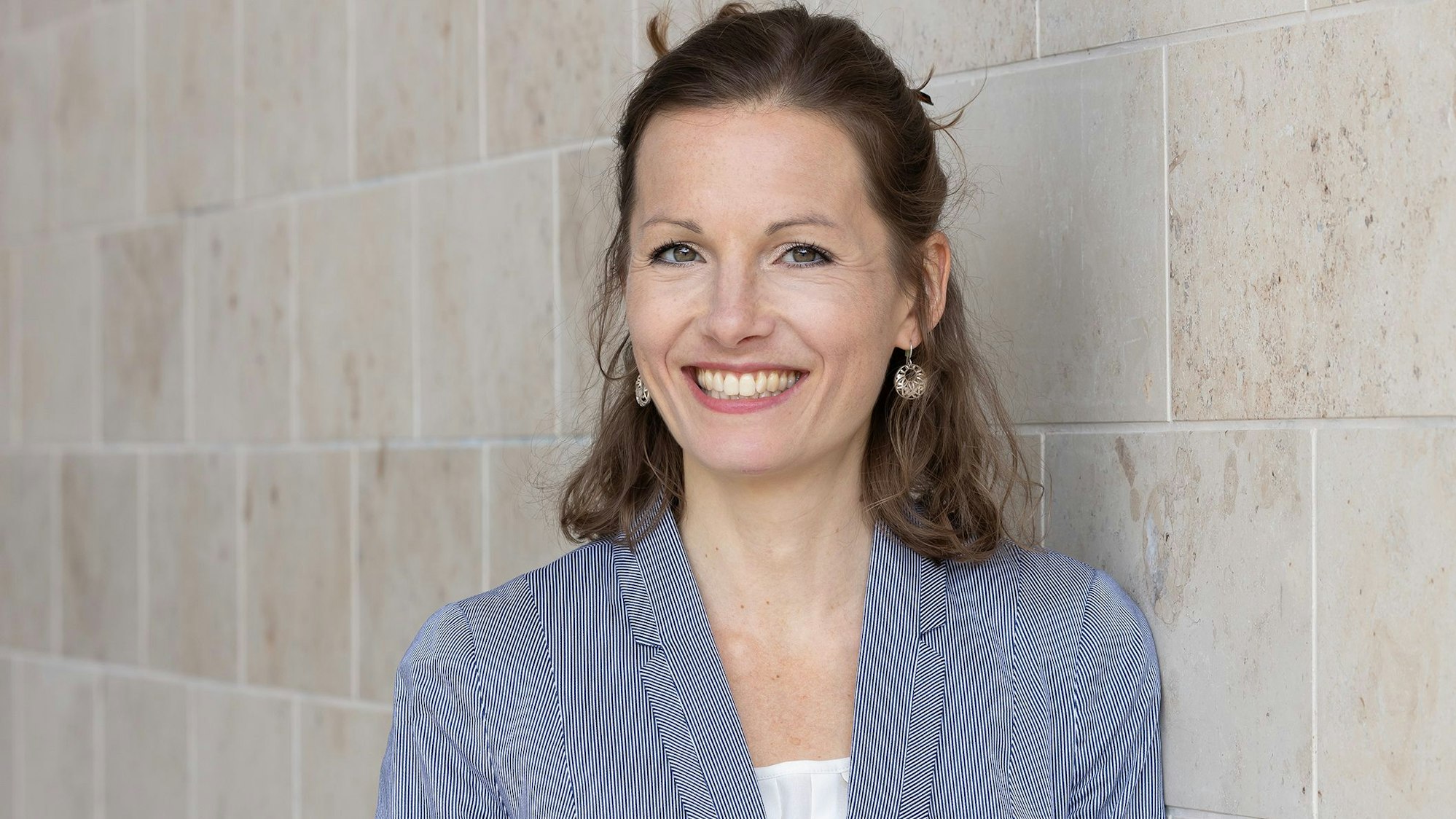 Professorin Henrike von Scheliha steht vor einer gekachelten Mauer und lächelt.
