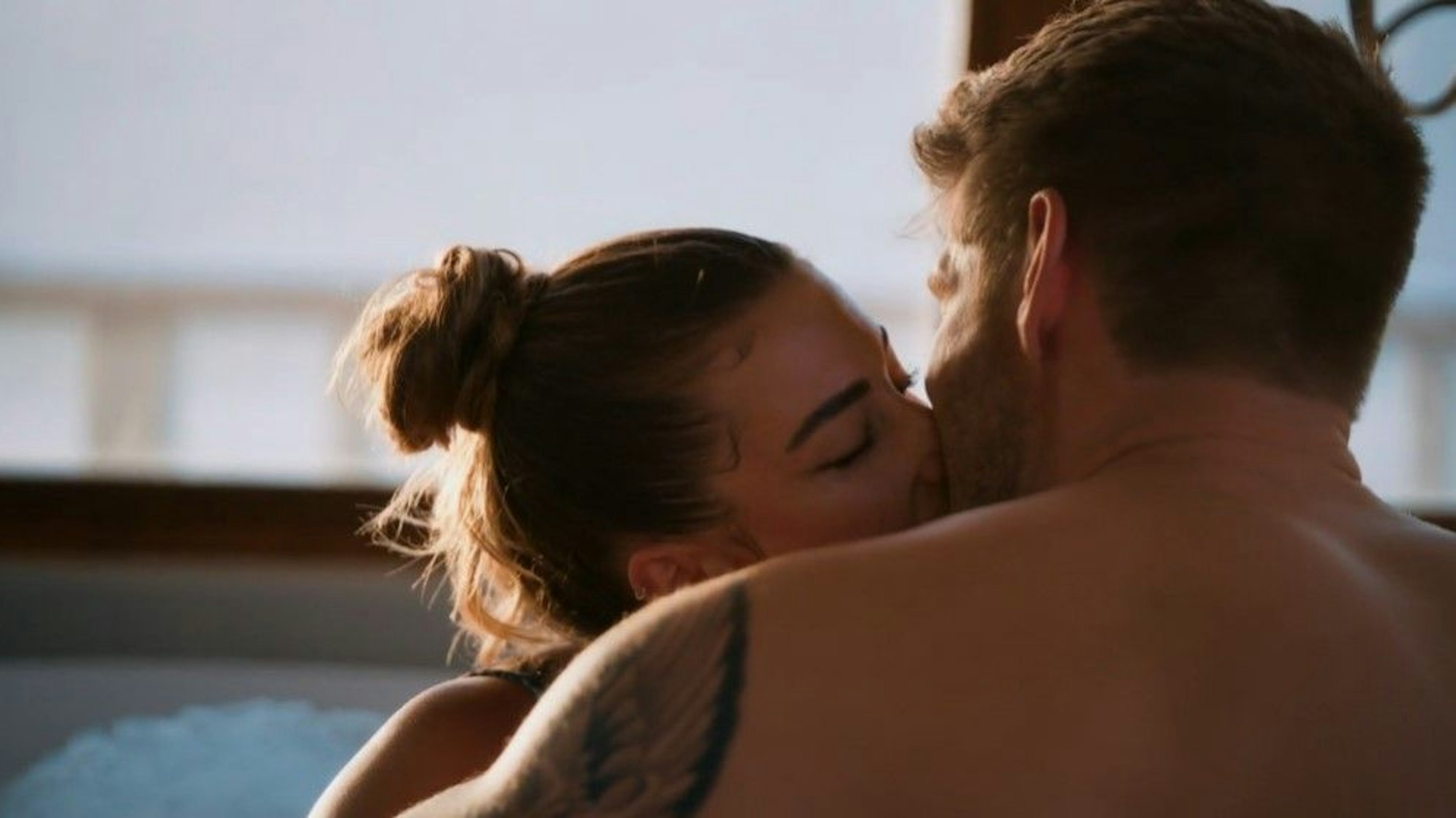 Lena und Martin küssen sich innig in einer Badewanne.