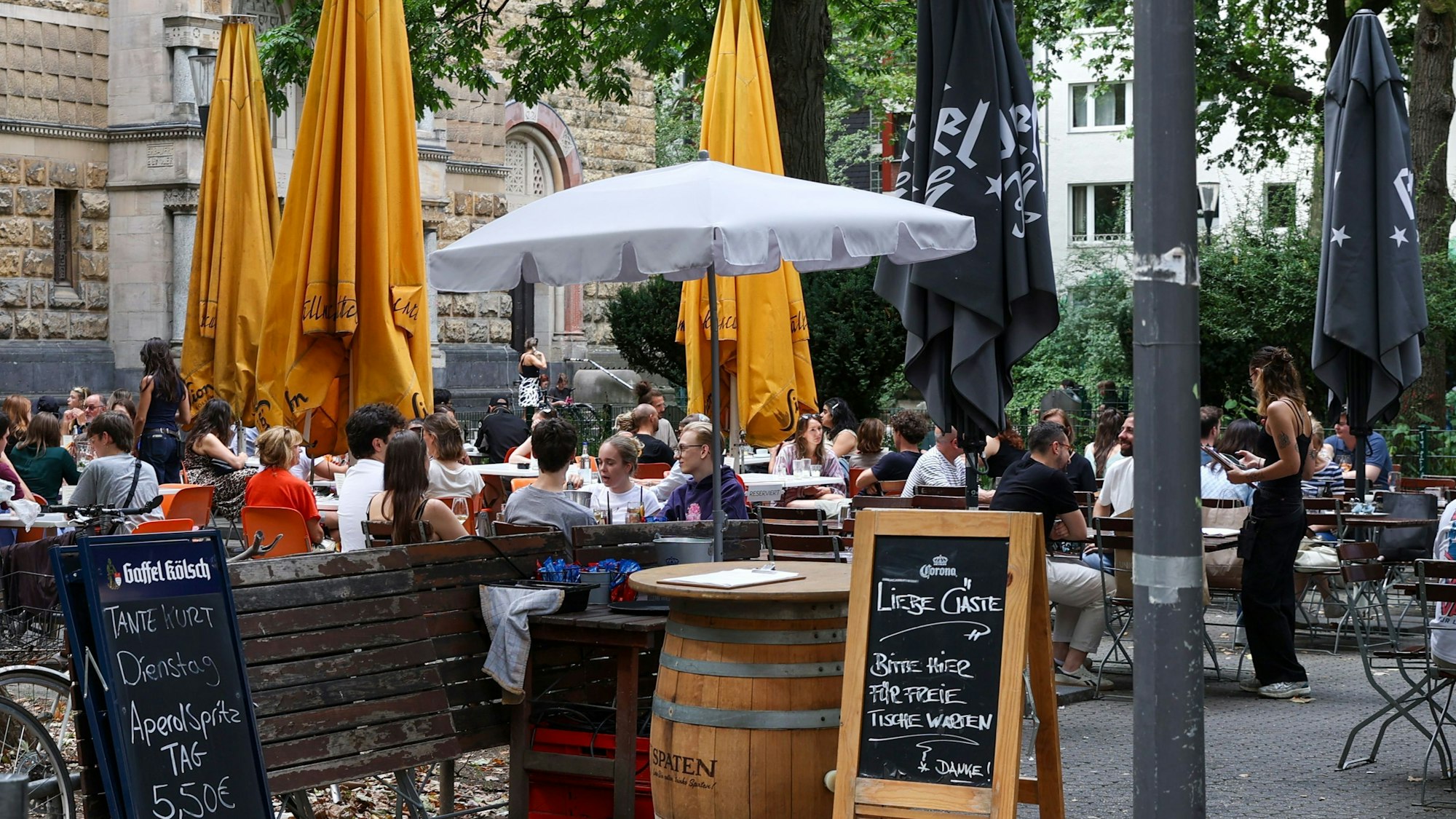 Menschen sitzen an Tischen der Außengastronomie am Brüsseler Platz.