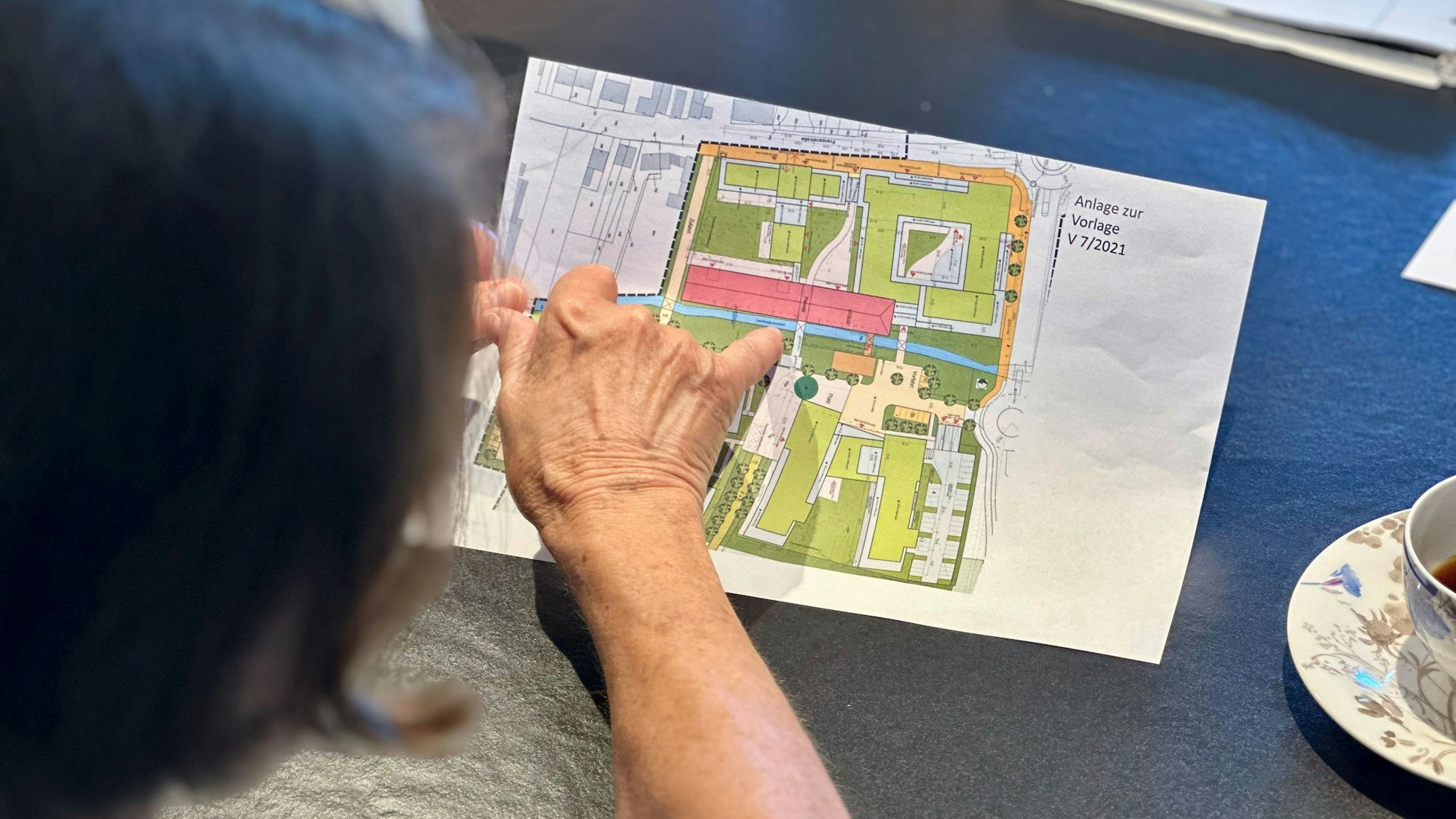 Eine Frau beugt sich über einen Plan und zeigt mit dem Finger auf etwas auf dem Plan.