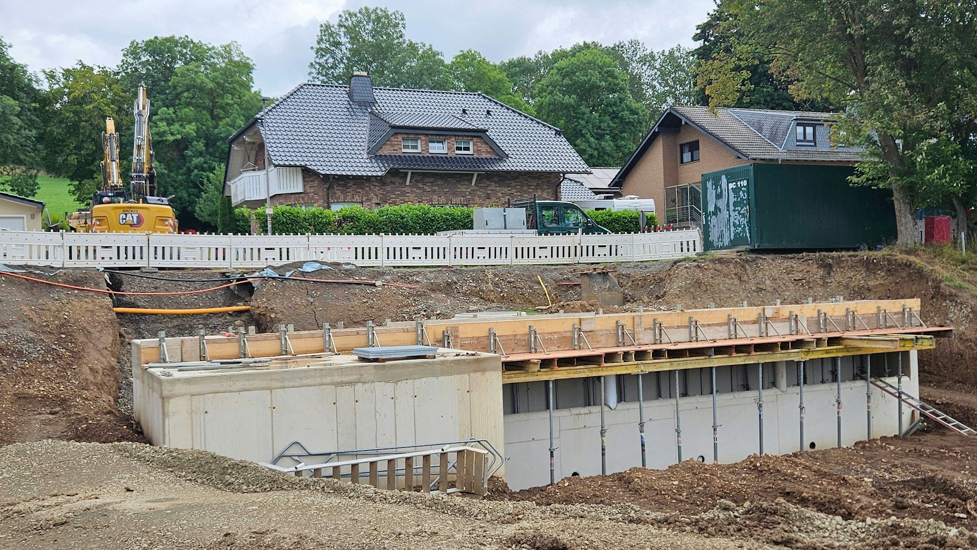 Unterhalb von zwei Wohnhäusern ist ein rechteckiges Betonbauwerk mit mehreren Öffnungen zu sehen.
