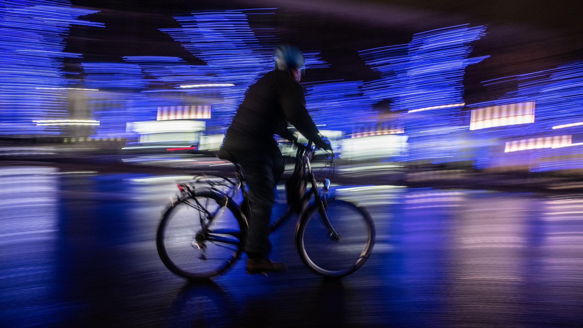 Ein Radfahrer fährt am Abend an illuminierten Bäumen auf der Straße.