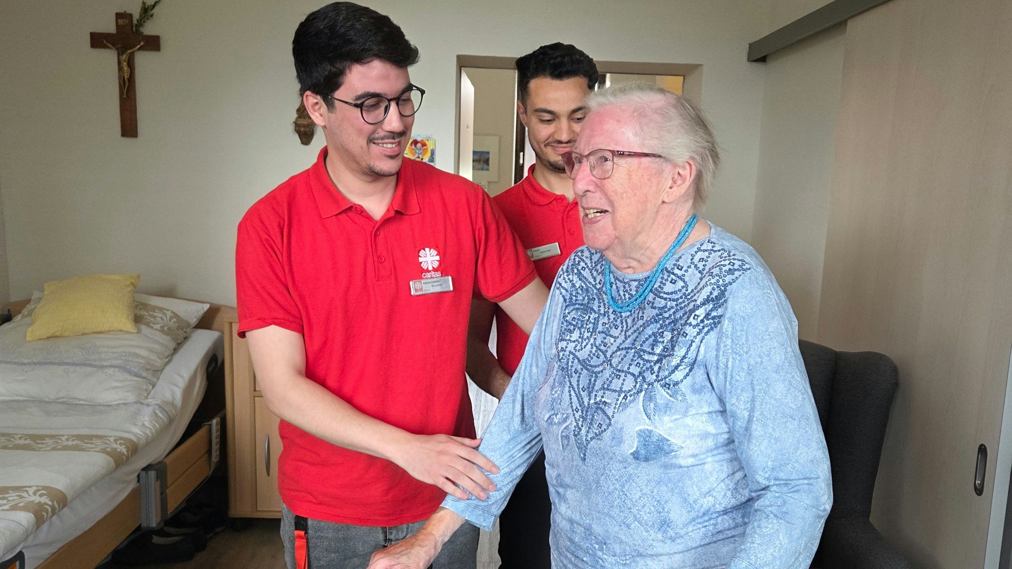 Die Caritas Rhein-Sieg bildet in Kooperation mit Sprachschulen Pflegekräfte aus Marokko in Deutschland aus. Das Projekt zeigt sich erfolgreich. Die beiden Auszubildenden Reda Gannour (links) und Abderrahim Boudra (rechts) helfen einer Bewohnerin mit ihrem Rollator.
