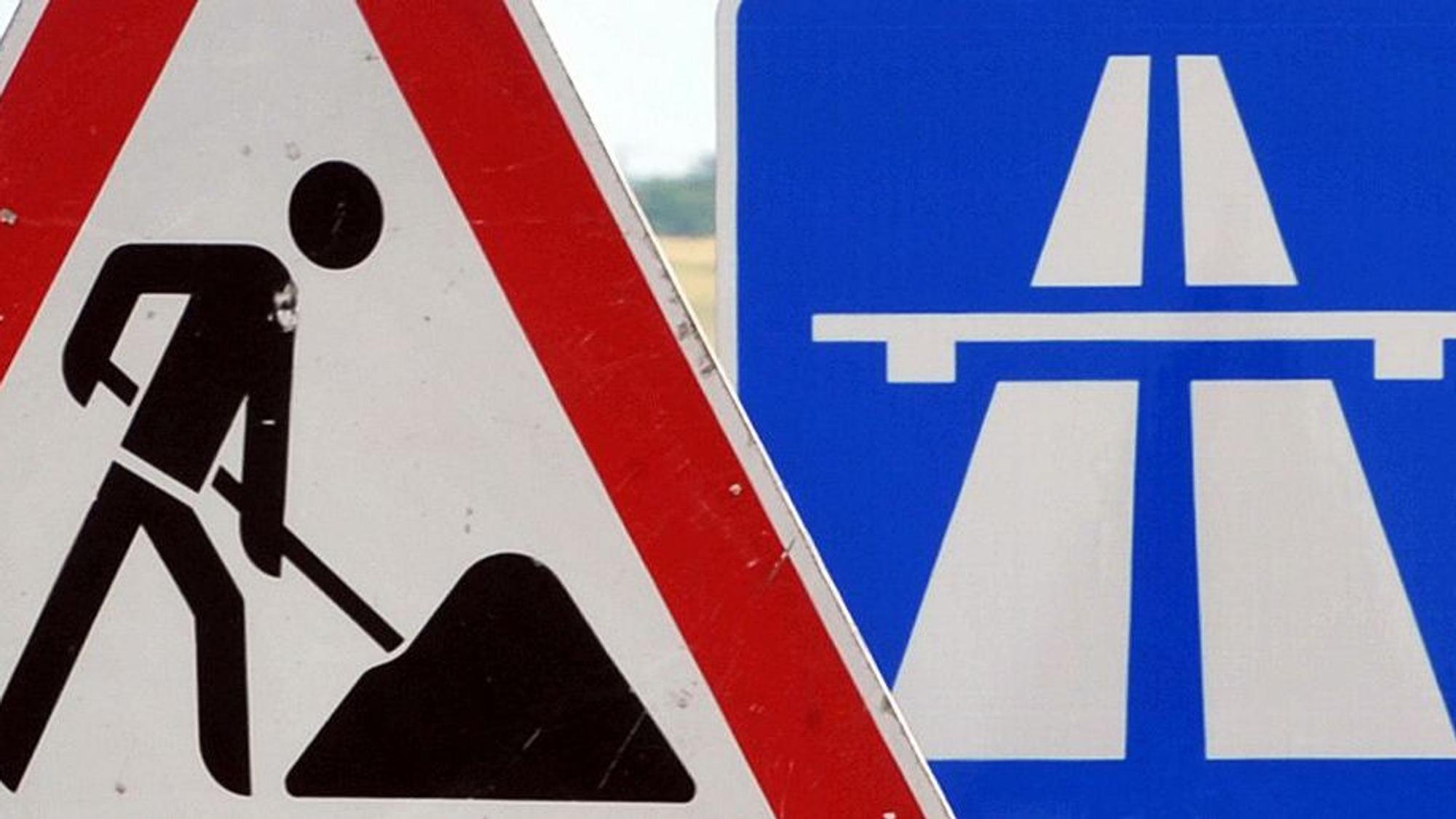 Ein Baustellenschild ist vor einem Autobahnschild platziert.