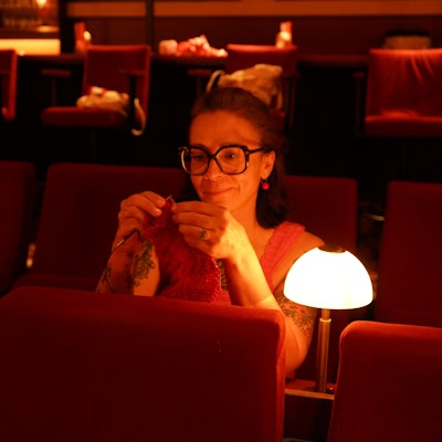 Das Foto zeigt eine strickende Frau im Kino.
