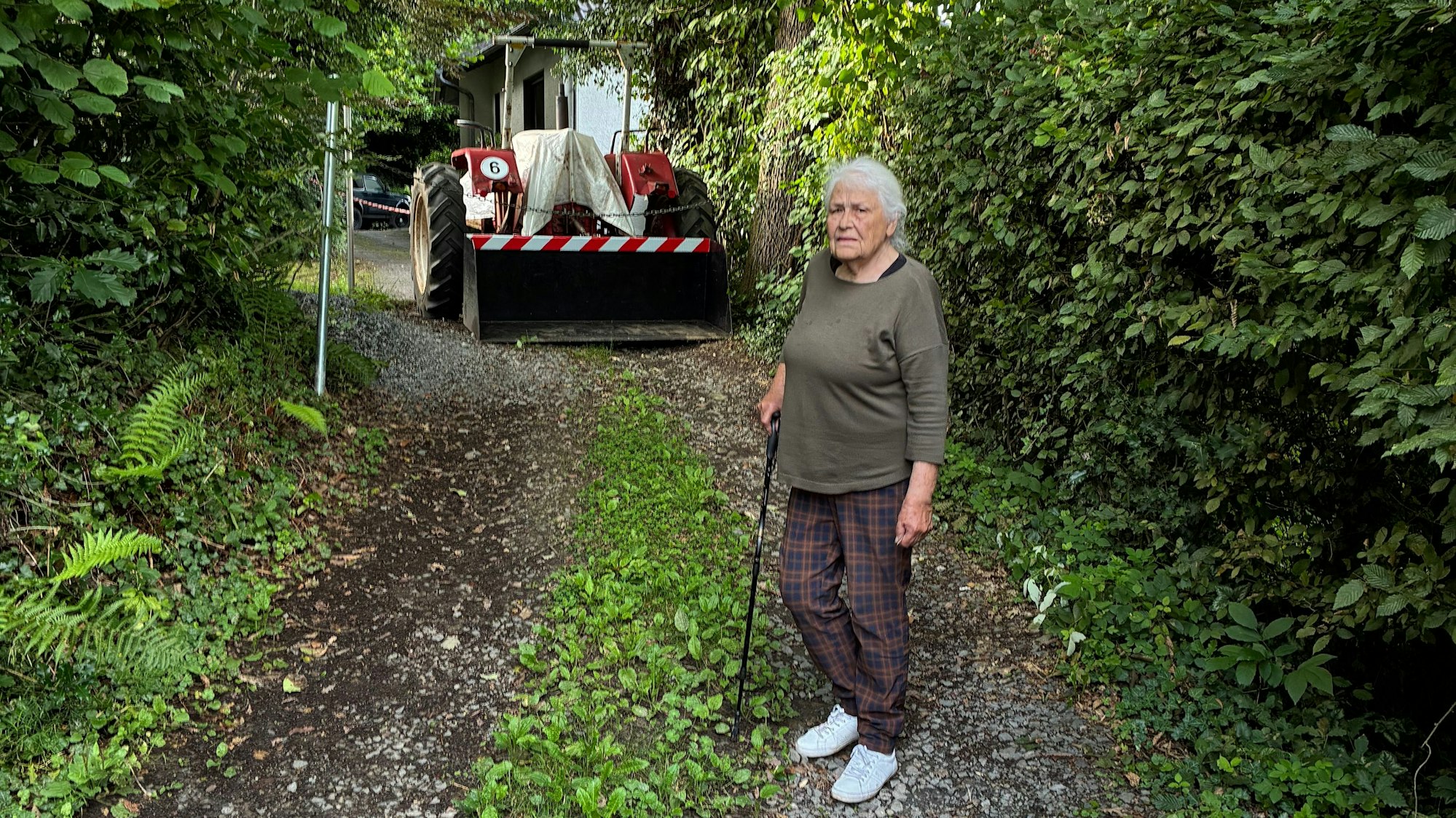 Irmintraut Fuchs steht, gestützt auf einen Stock, vor der Eisenkette und dem Trecker, die ihr den Weg zu ihrem Grundstück versperren.