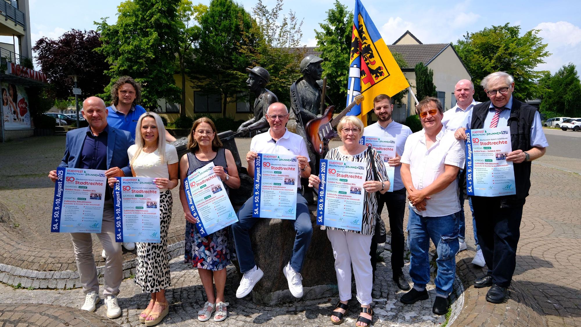 Programmvorstellung Brunnenfest: Das Orga-Team posiert mit Fahne und Plakaten am Mechernicher Marktplatz.