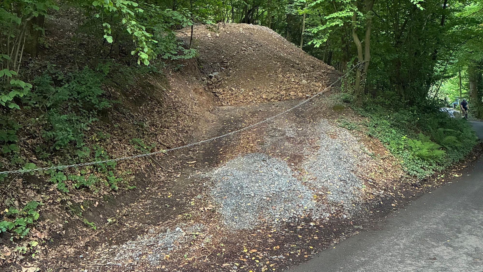 Ein Weg mit Erde und Schotter wird durch eine Kette versperrt.