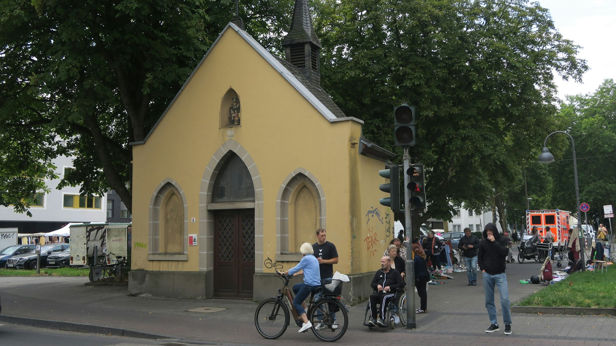 An einer Straße steht eine Kapelle mit beigem Anstrich, der mit Graffiti beschmiert ist.