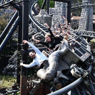 Das Foto zeigt die Ministerin mit hochgerissenen Armen vorn in einem voll besetzten Zug der Achterbahn, der sich gerade in die Kurve legt.