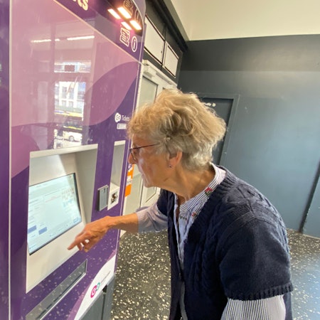 Eine ältere Dame steht an einem Ticketautomaten und schaut konzentriert auf das Display.