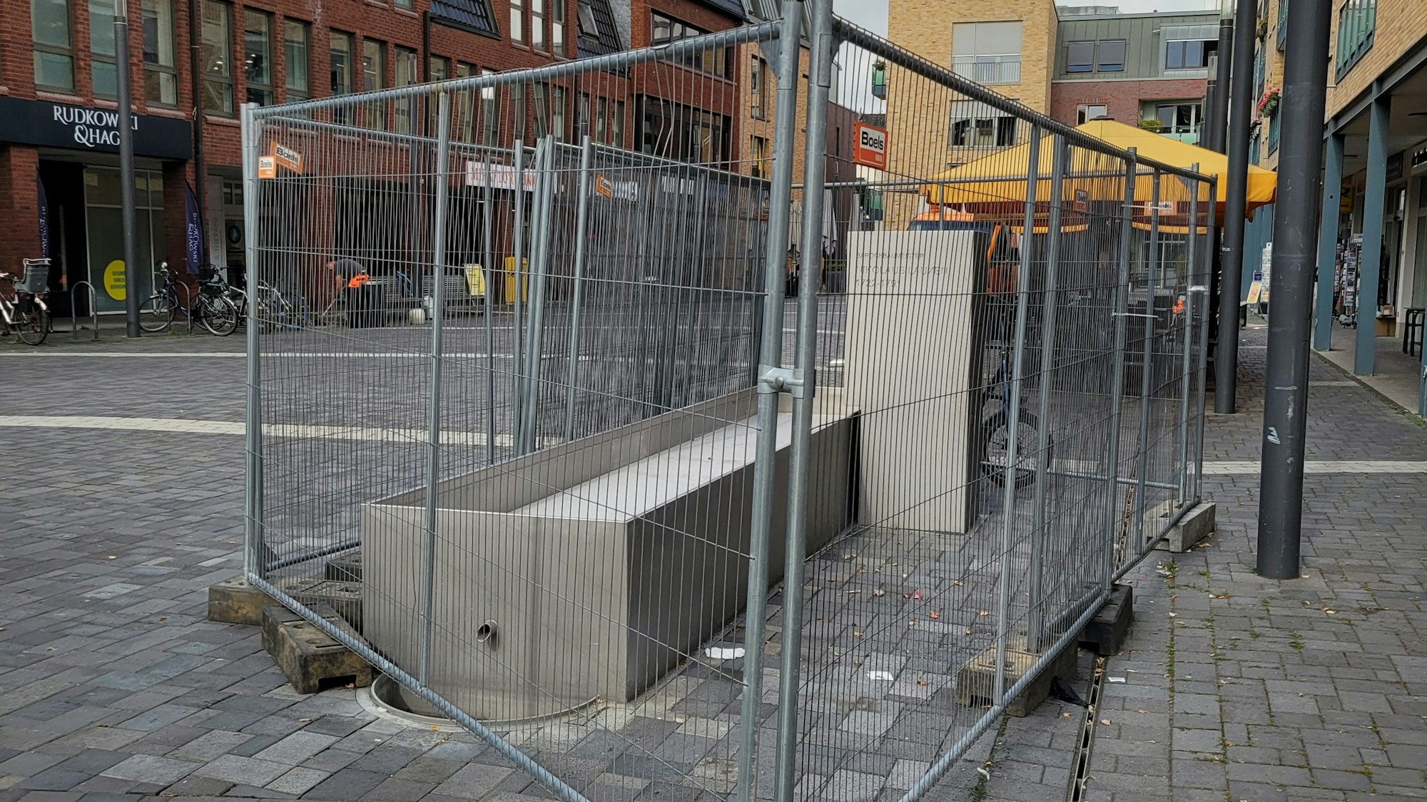 Das Bild zeigt den umzäunten Brunnen in der Pulheimer Innenstadt.