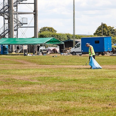 Mit Zange und Müllsack ist Nils auf dem Sportplatz unterwegs. Im Hintergrund sind der Aussichtsturm und das Festival-Gelände zu sehen.