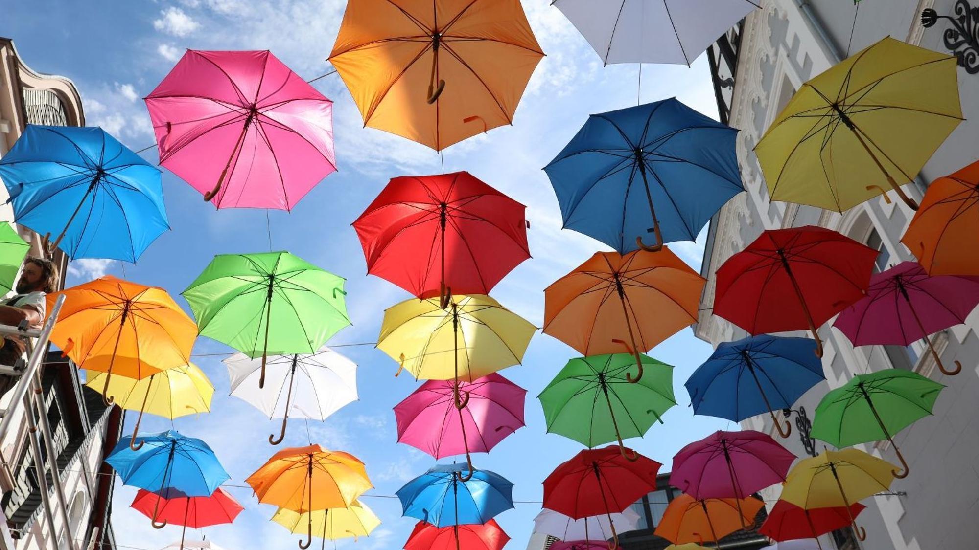 Bunte Regenschirme hängen an Drahtseilen über einer Straße-