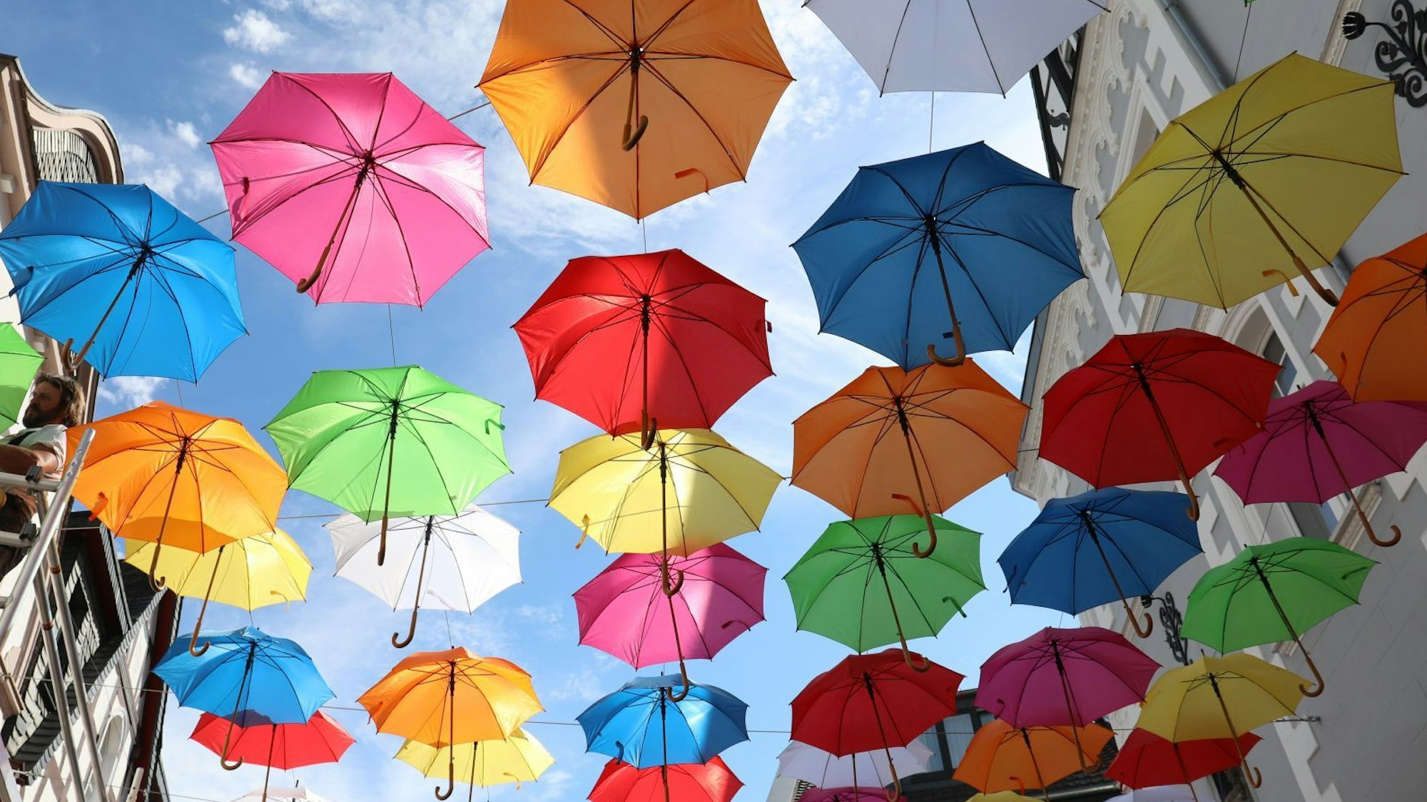 Bunte Regenschirme hängen an Drahtseilen über einer Straße-