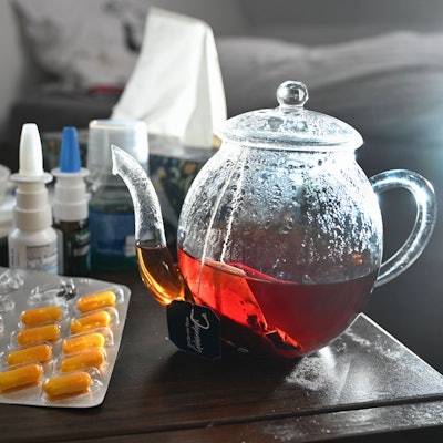 Medikamente und eine Kanne Tee zur Bekämpfung einer Erkältung sind auf einem Nachttisch aufgestellt.