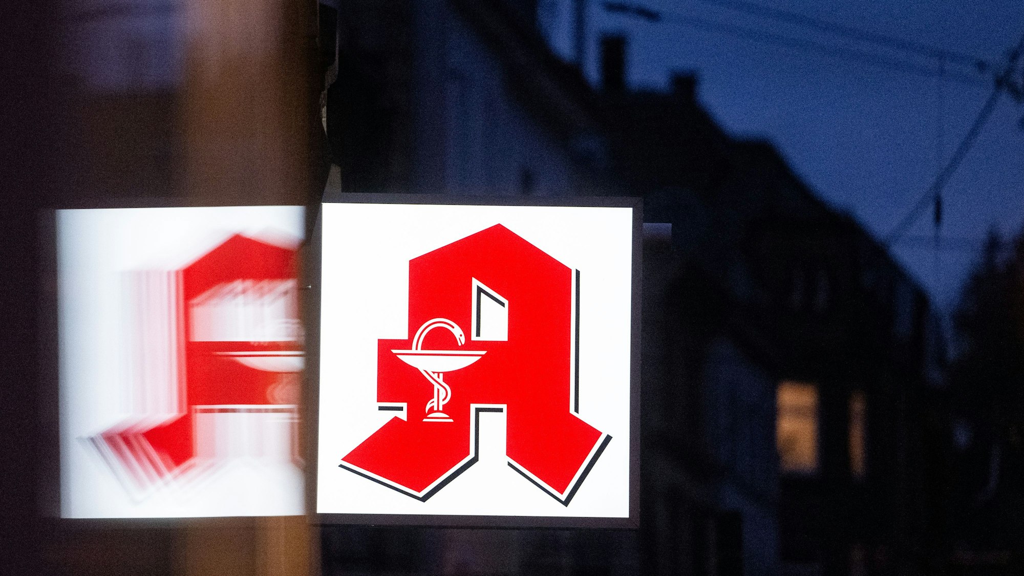 Ein Apothekenschild leuchtet an der Fassade eines Gebäudes.
