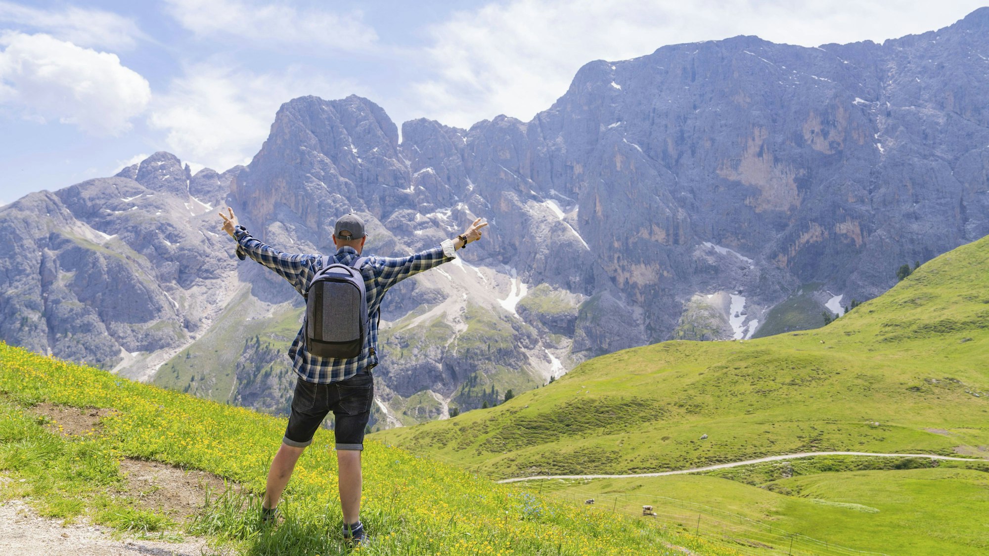 Ein Wanderer mit erhobenen Armen blickt zu einer beeindruckenden Bergkulisse auf einer Wiese in den Dolomiten.
