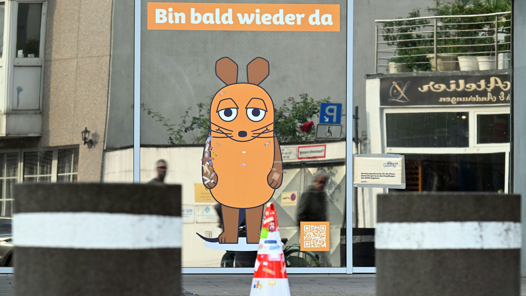05.08.2025, Nordrhein-Westfalen, Köln: «Bin bald wieder da» steht über einem Maus-Aufkleber an einem WDR-Gebäude. Die orangefarbene Maus-Figur wurde bei einem Brandanschlag beschädigt. Nun wird geprüft, ob sie repariert werden kann oder ganz ersetzt werden muss. Foto: Federico Gambarini/dpa +++ dpa-Bildfunk +++